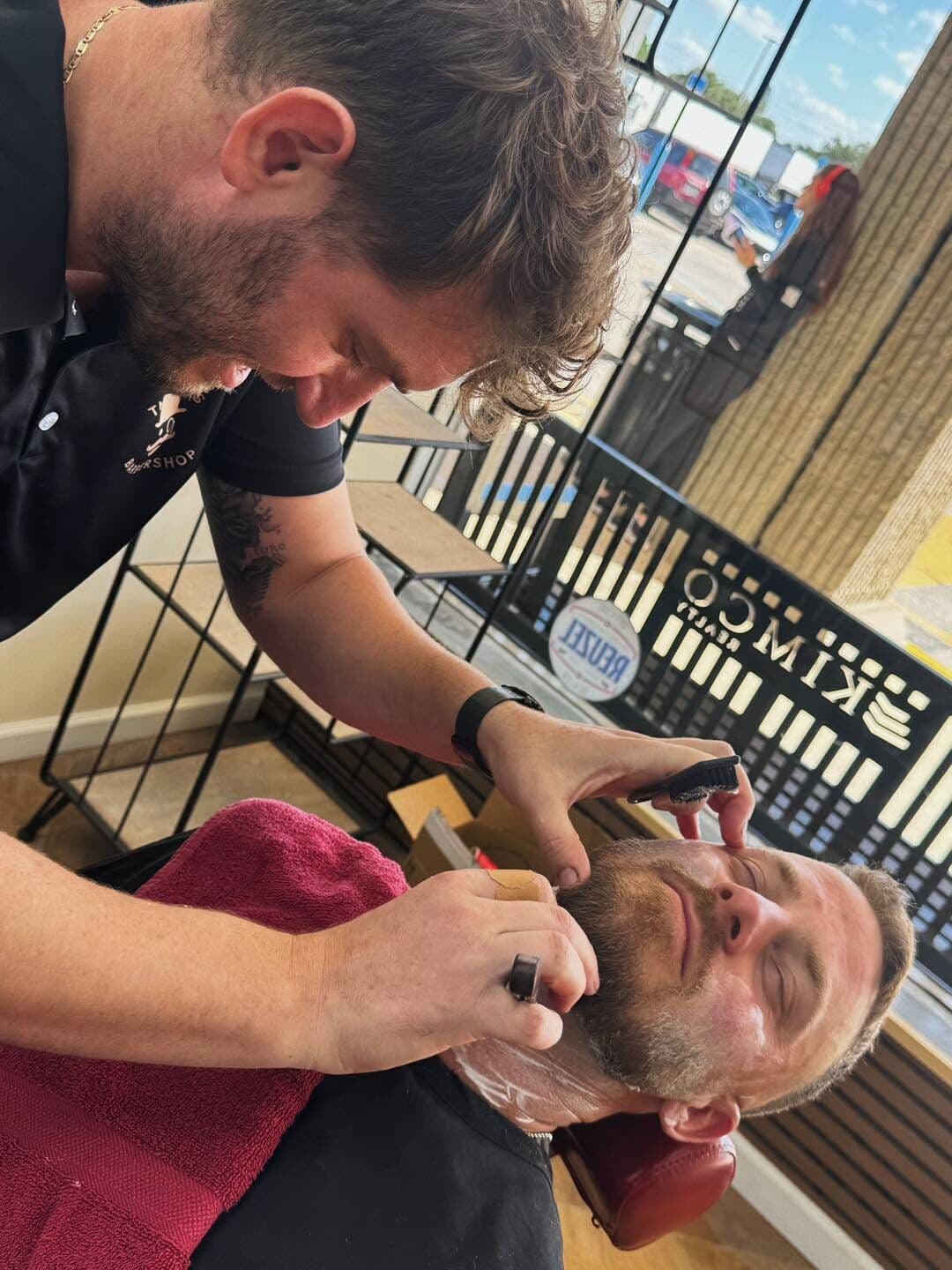 Andy Peto lining up a reclined client's beard with a razor