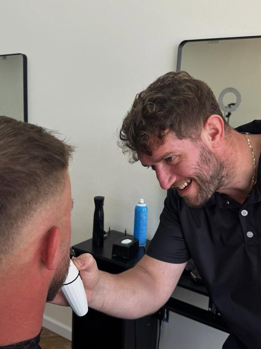 Andy Peto smiling as he blends a client's fade with clippers