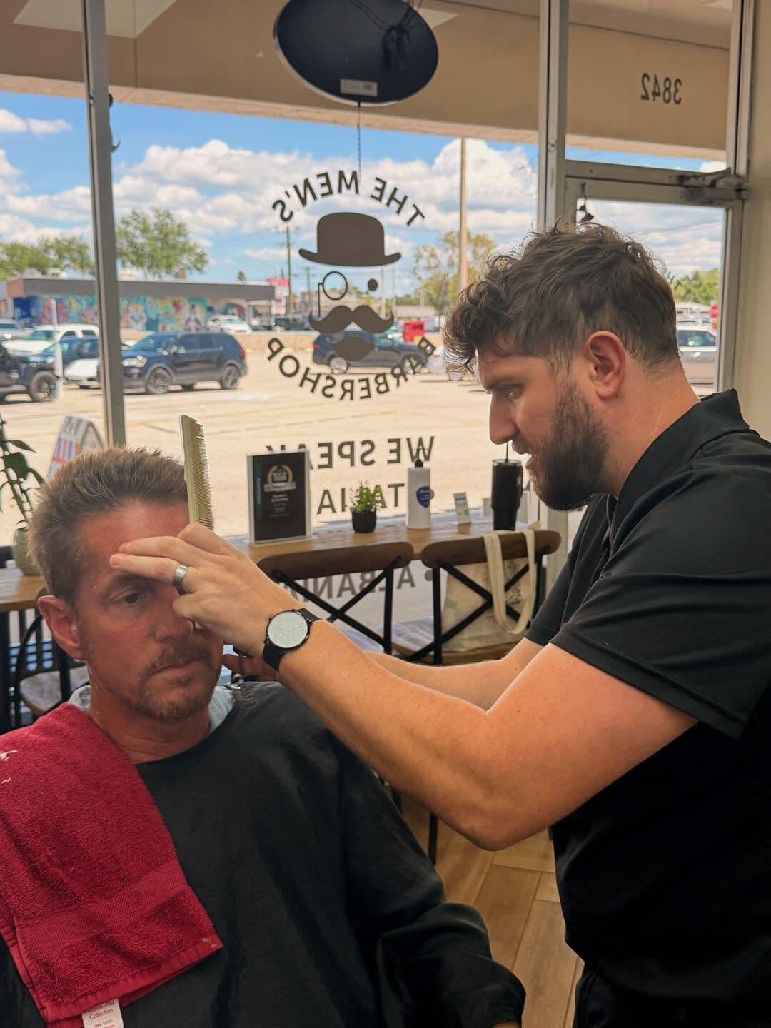 Andy Peto combing through a client's hair at the front window, with the shop's logo on the glass