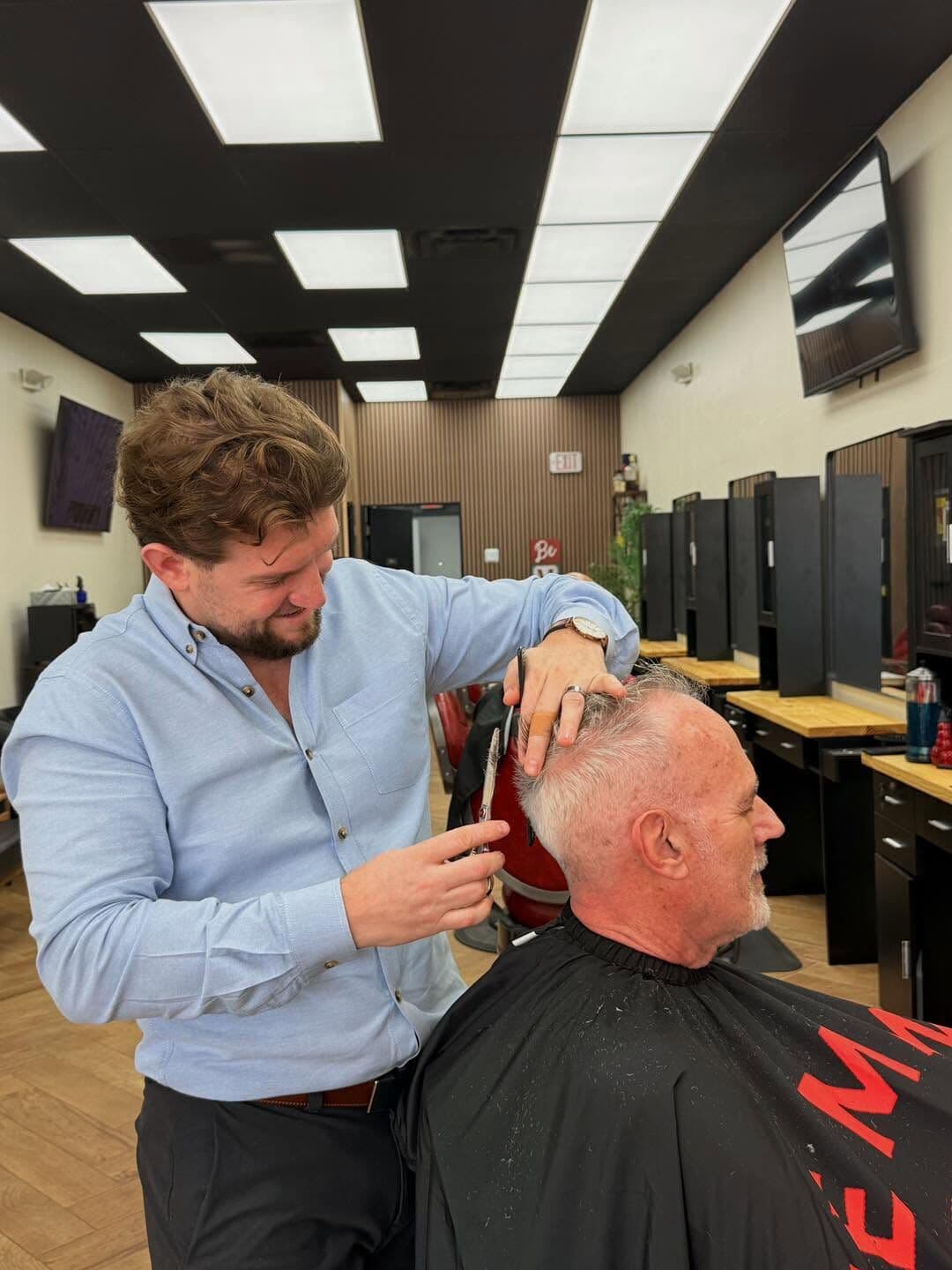 Andy Peto trimming a client's white hair with scissors