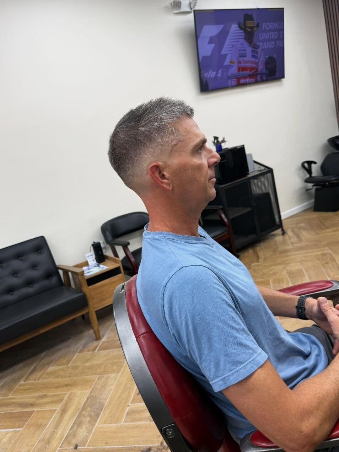 A client with gray hair cut short into a fade, in profile in a red barber chair
