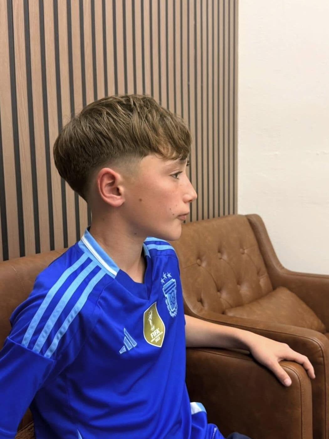 A boy with a textured fringe and a low taper after his haircut at The Men's Barbershop