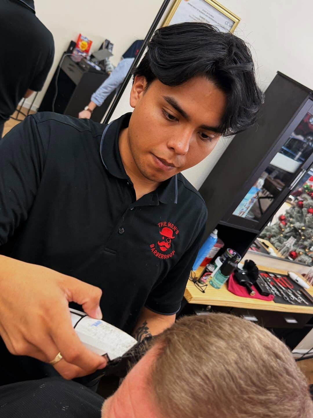 Moises cutting a client's hair with clippers at his station