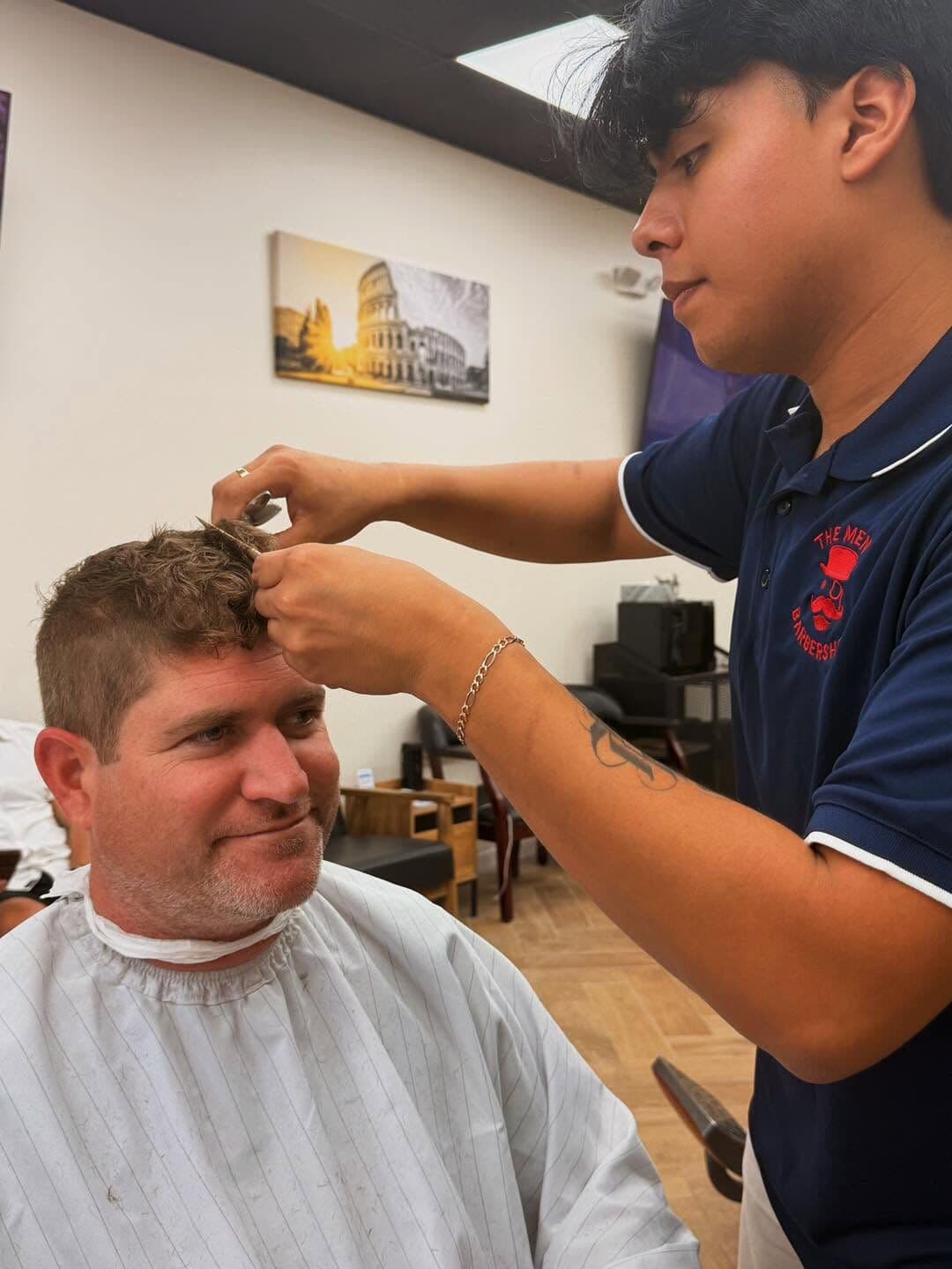 Moises trimming the top of a smiling client's hair with scissors
