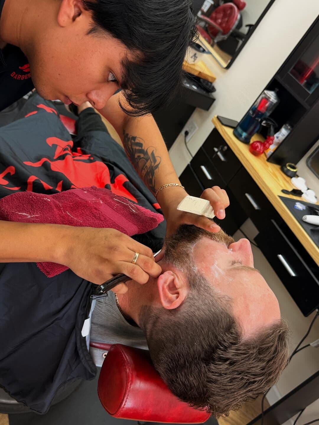 Moises lining up a reclined client's beard with a straight razor