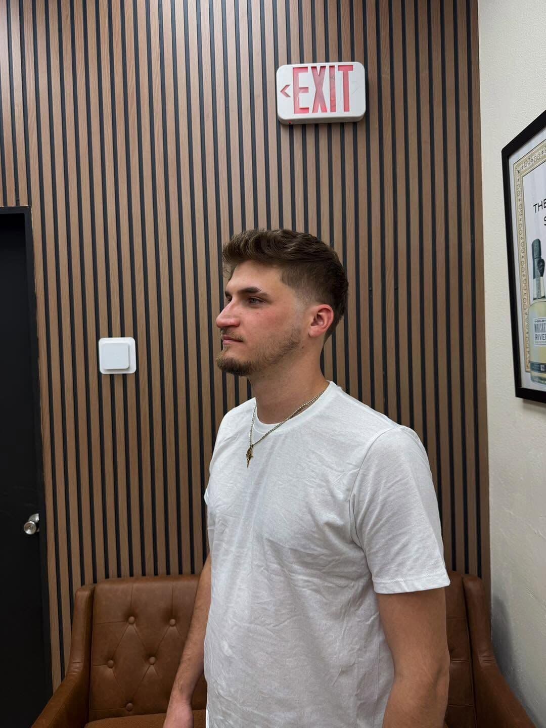A client with a textured crop and a mid fade, standing by the wood-slat wall
