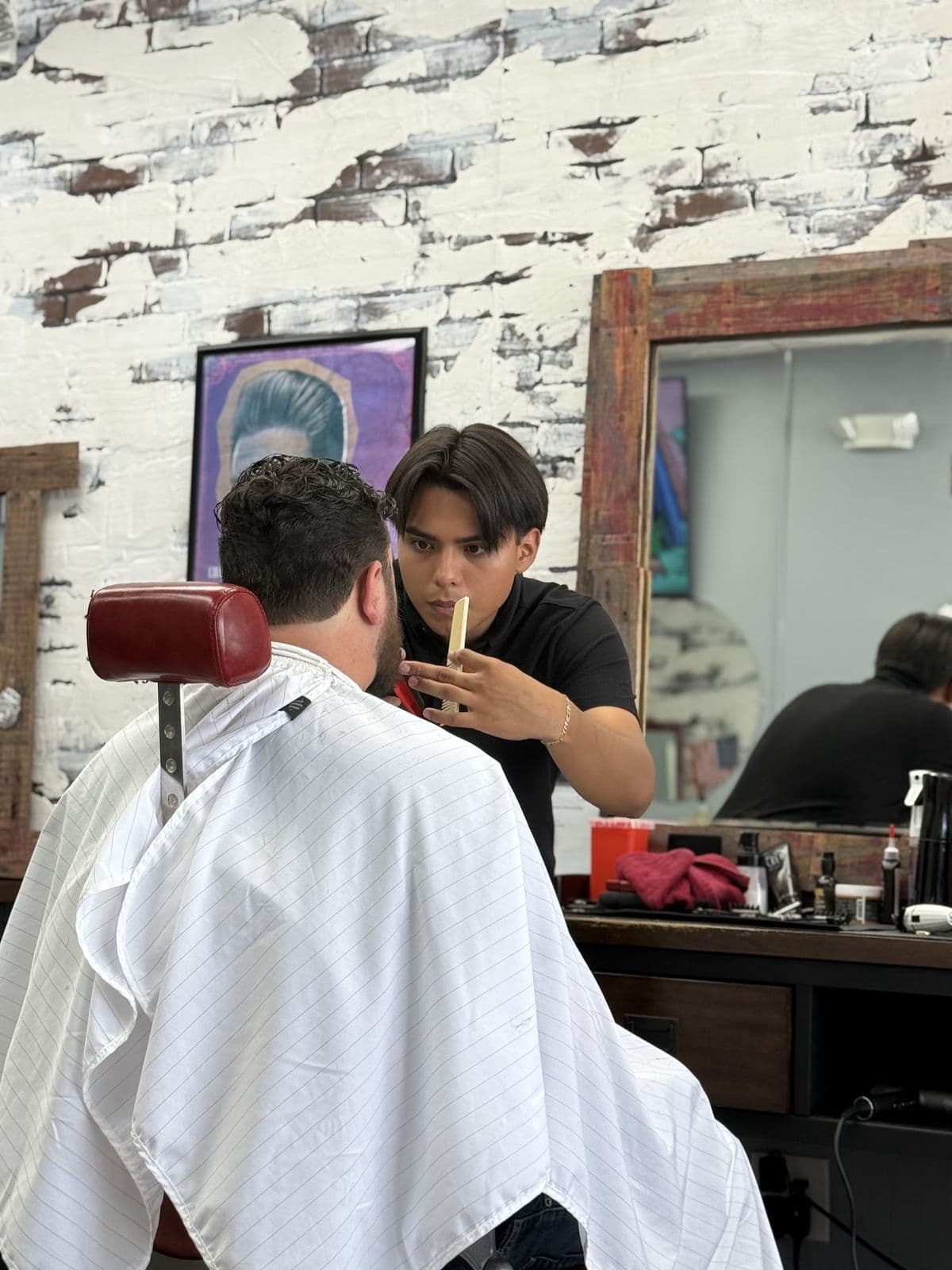 A barber working on a client's beard with a razor at The Men's Barbershop