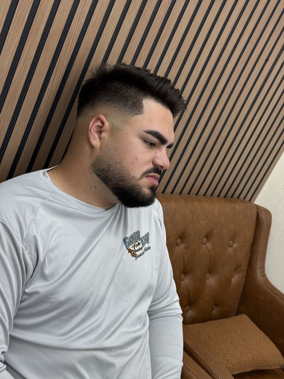 A client with a high fade and a full, shaped beard, in a leather chair