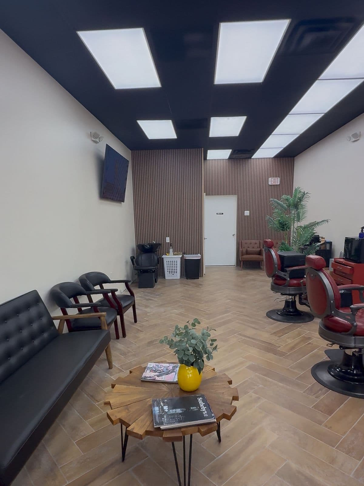 The waiting area: a black leather sofa, a wood-slab table and the red barber chairs